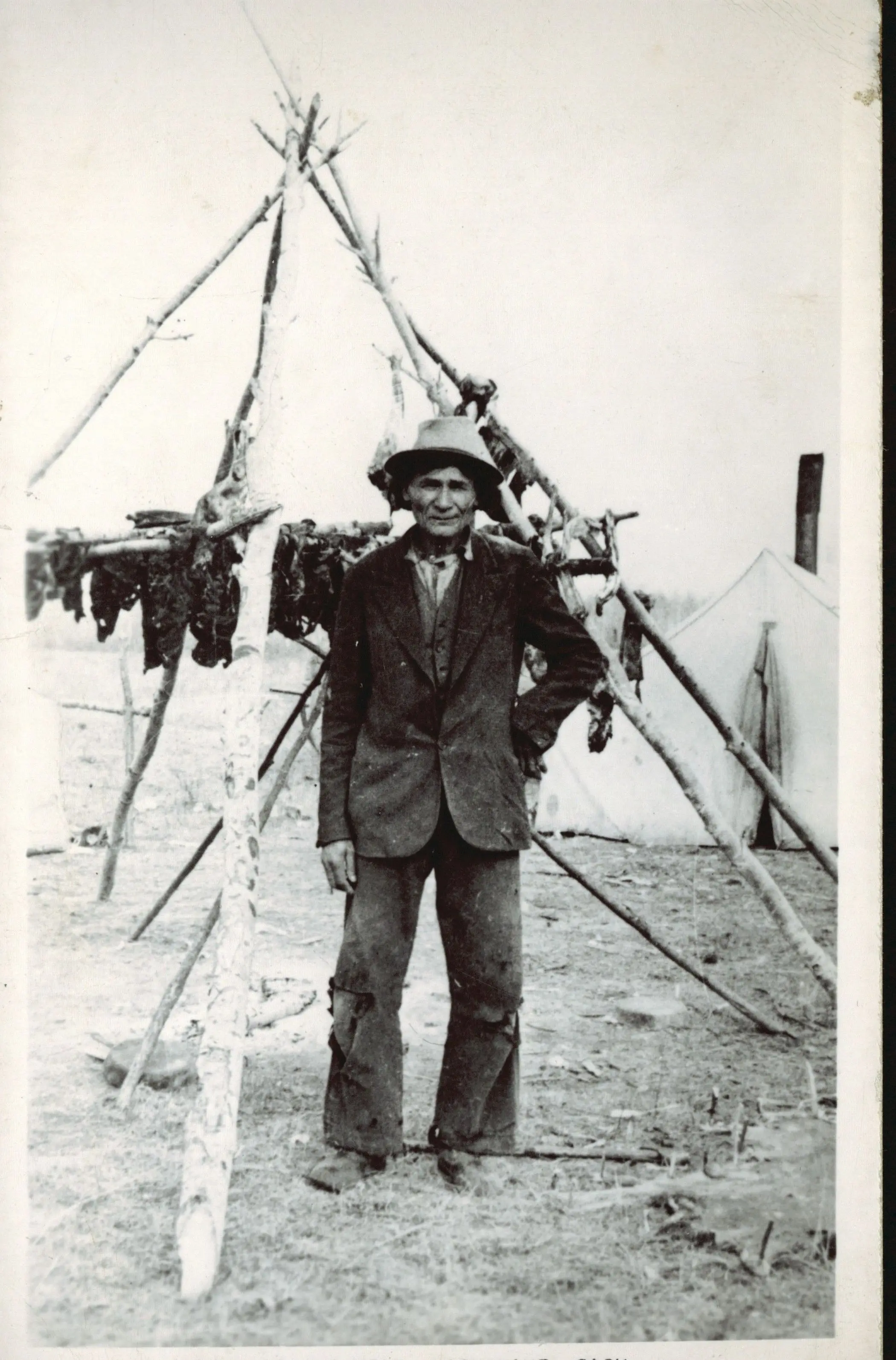 Man beside a meat-drying rack, Loon Lake